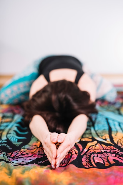 Young woman practicing stretching exercise on colorful blanket