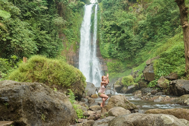 Молодая женщина, практикующих йогу у водопада