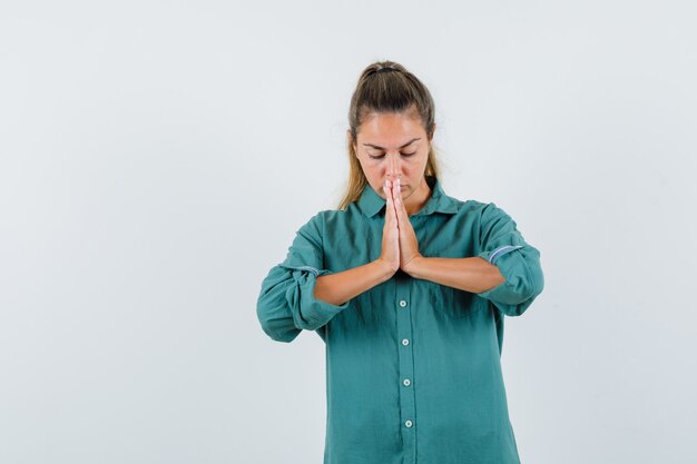 Young woman praying for something in blue shirt and looking focused
