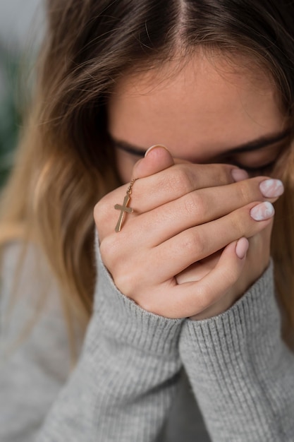 Free photo young woman praying while holding cross necklace