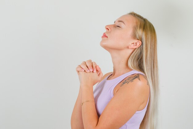 Young woman praying with clasped hands in singlet and looking hopeful
