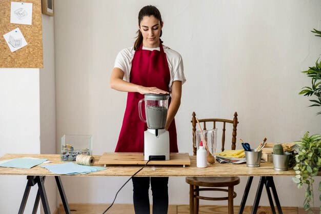 Young woman preparing paper pulp in mixer at workshop