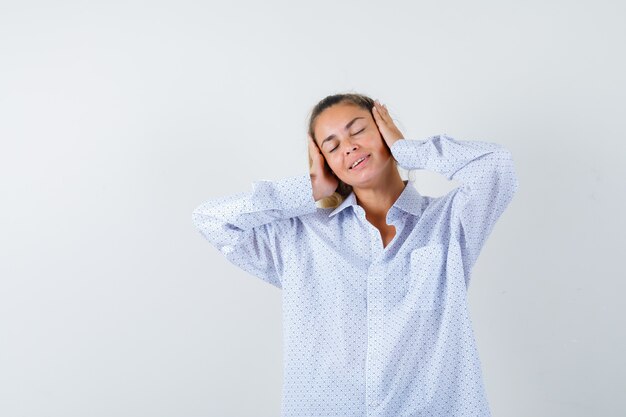 Young woman pressing hands on ears, keeping eyes closed in white shirt and looking happy