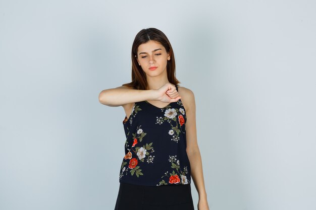 Young woman pretending to look at watch on her wrist in blouse, skirt and looking pensive. front view.