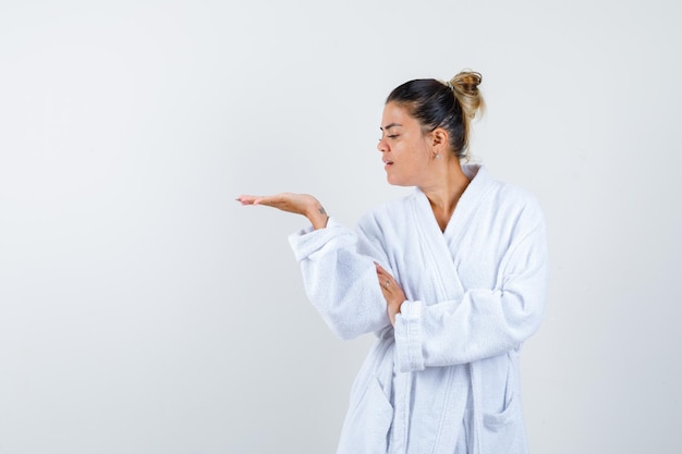 Young woman pretending to show something in bathrobe and looking confident