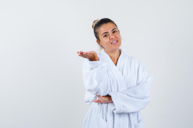 Young woman pretending to show something in bathrobe and looking confident