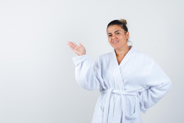 Young woman pretending to show something in bathrobe and looking confident