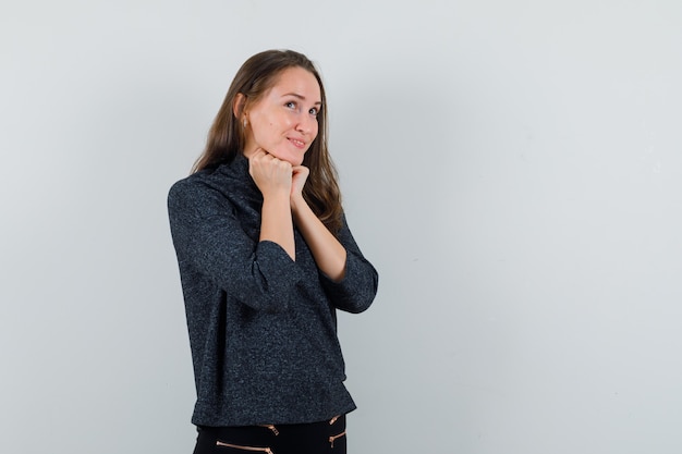 Young woman propping chin on fists in shirt and looking dreamy 