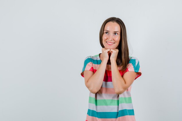 Young woman propping chin on fists in t-shirt and looking hopeful , front view.