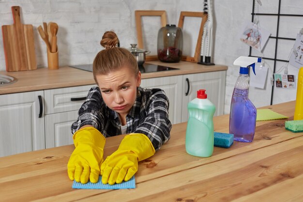 Young woman in protective gloves wipes a table in the kitchen with a rag. Fatigue. Household, cleaning and people concept