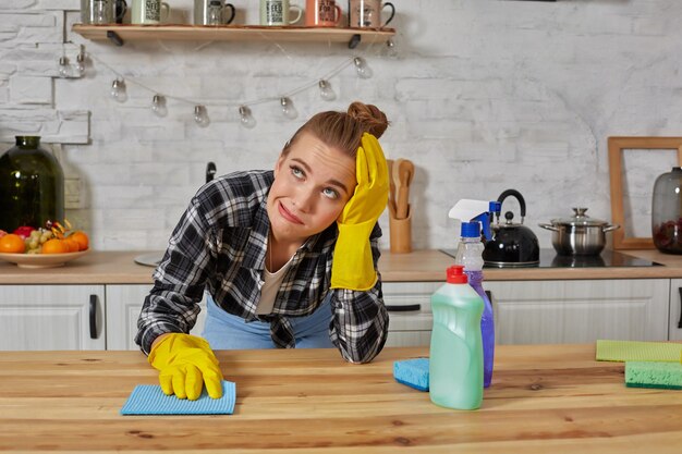保護手袋をはめた若い女性が台所のテーブルを雑巾で拭きます。倦怠感。家庭、掃除、人々 の概念