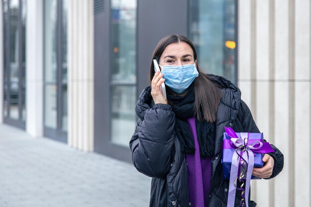 Молодая женщина в защитной маске с подарком в руках разговаривает по телефону