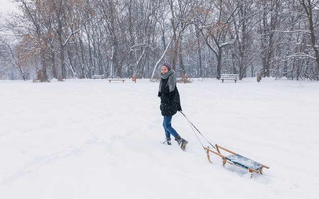 森で雪の風景に空の木製そりを引く若い女性