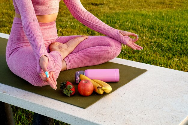 young woman in purple shirt and trousers on the grass during daytime inside green park meditating yoga bottle