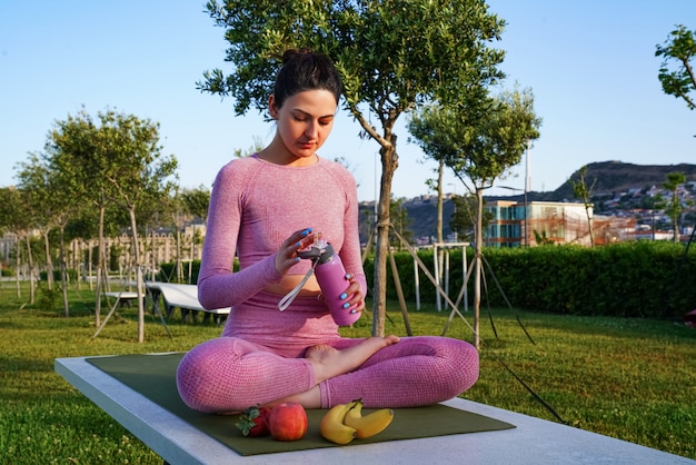 緑の公園の瞑想中の昼間の間に紫色のシャツとズボンの芝生の上の若い女性