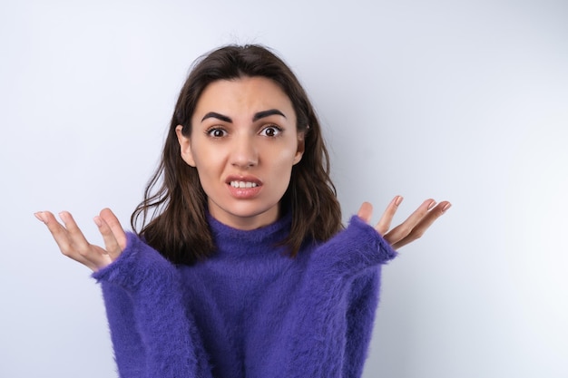 Молодая женщина в фиолетовом мягком уютном свитере на заднем плане потрясена, смущена и недоверчиво пожимает плечами.