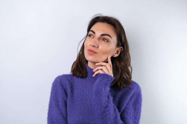Молодая женщина в фиолетовом мягком уютном свитере на заднем плане задумчиво думает об идеях, смотрит в сторону