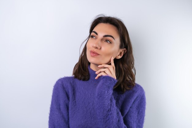 Young woman in a purple soft cozy sweater on the background thoughtful thinking  of ideas look aside