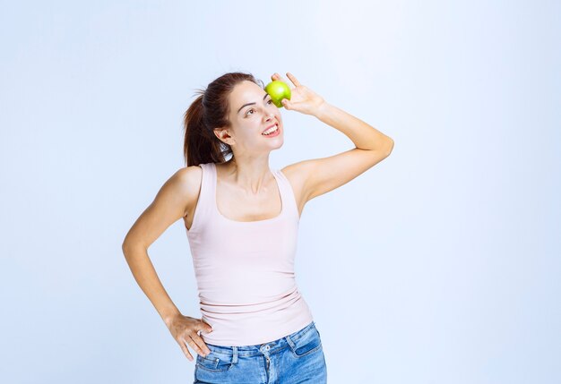 Young woman putting a green apple to her eye