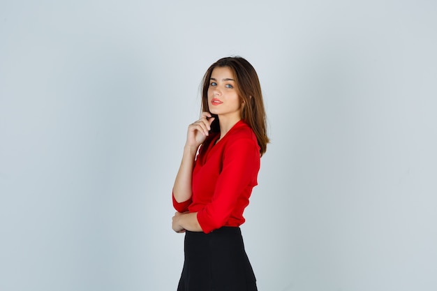 Young woman putting hand under chin, looking over shoulder in red blouse