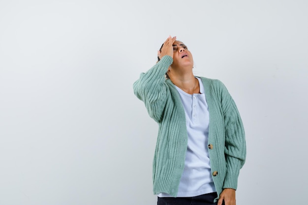 Foto gratuita giovane donna che mette la mano sulla testa, guarda sopra in camicia bianca e cardigan verde menta e sembra concentrata