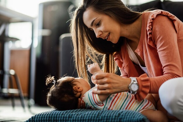 Young woman putting her baby girl on the pillow while enjoying with her at home