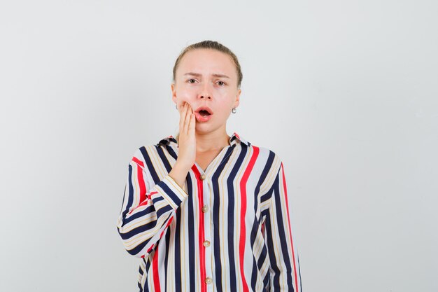 Young woman putting her hand on cheek in striped blouse and looking shocked