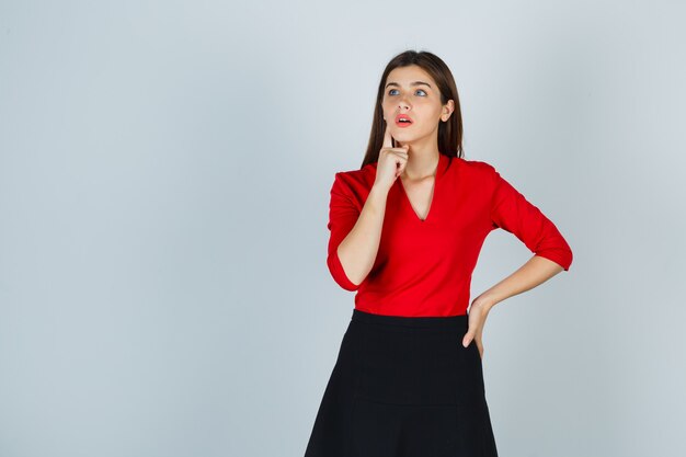 Young woman putting index finger near mouth, thinking about something