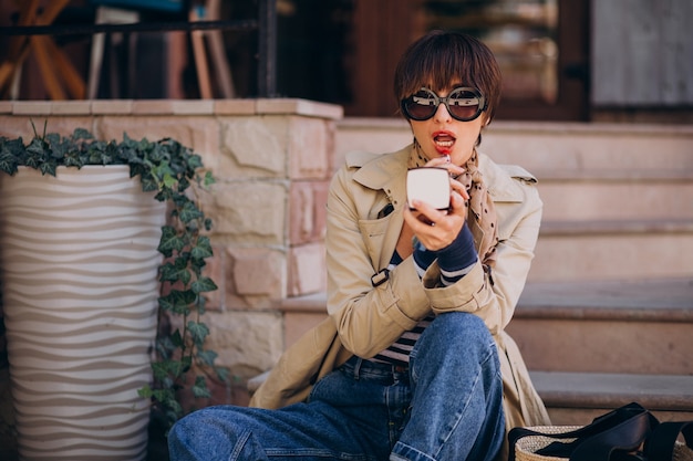 Young woman putting on lipstick in the street