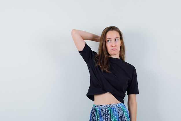 Young woman putting one arm behind head while looking away in black t-shirt and blue skirt and looking pensive