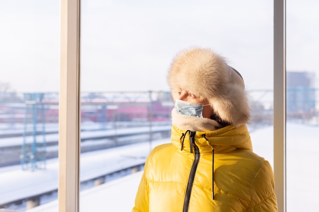 Free photo young woman at the railway station in a protective mask on the face in winter clothes passenger