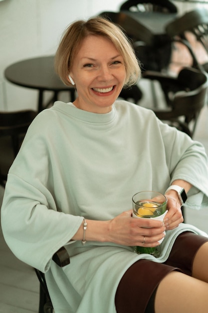 A young woman in the rain on an open terrace drinks tea from a large glass