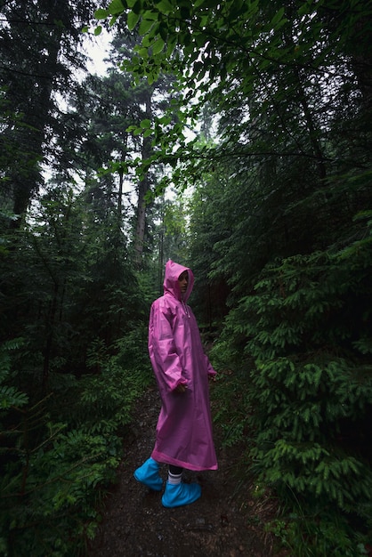 비옷을 입은 젊은 여성이 빗속에서 숲을 걷는다