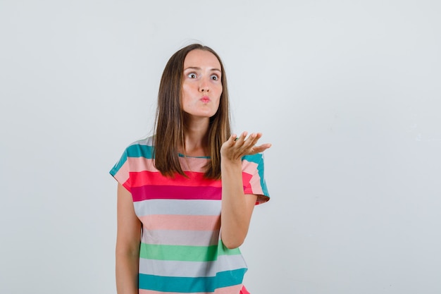 Young woman raising hand in aggressive manner in t-shirt and looking angry , front view.