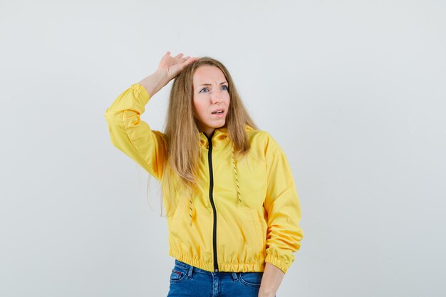 노란색 폭격기 재킷과 블루 진에 머리 위에 손을 올리고 매력적인 찾고 젊은 여자. 전면보기.