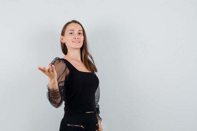 Young woman raising hand with open palm in black blouse and looking arrogant 