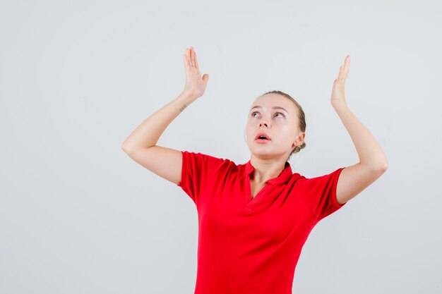 Young woman raising hands as holding something over head in red t-shirt