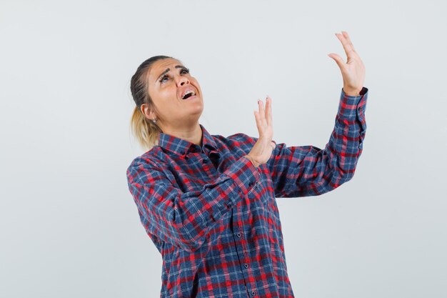Young woman raising hands like stopping something in checked shirt and looking stressed. front view.