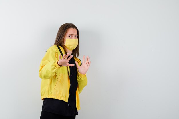 Young woman raising hands to stop and looking scared