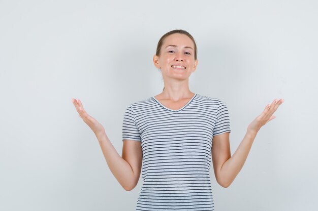 Young woman raising hands in striped t-shirt and looking grateful , front view.