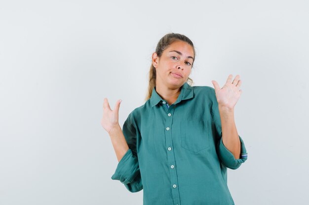 Young woman raising hands in surrender pose in green blouse and looking cute