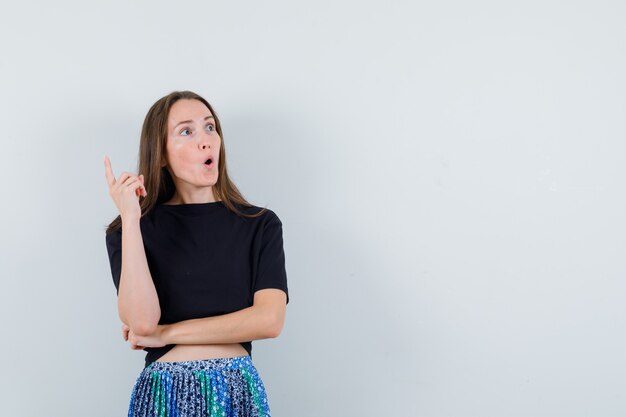 黒のTシャツと青いスカートでユーレカジェスチャーで人差し指を上げて、賢明に見える若い女性