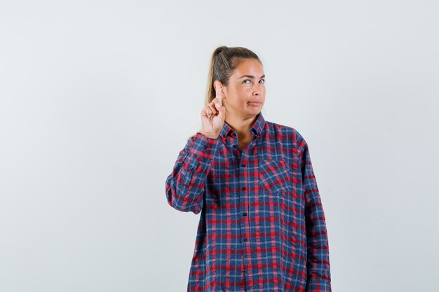 Foto gratuita giovane donna che alza il dito indice in gesto di eureka in camicia a quadri e guardando pensieroso