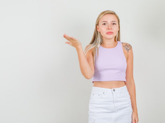 Young woman raising palm in singlet, mini skirt and looking annoyed