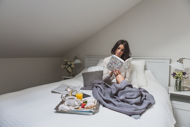 Free photo young woman reading a book on bed