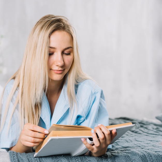 Young woman reading book on bed