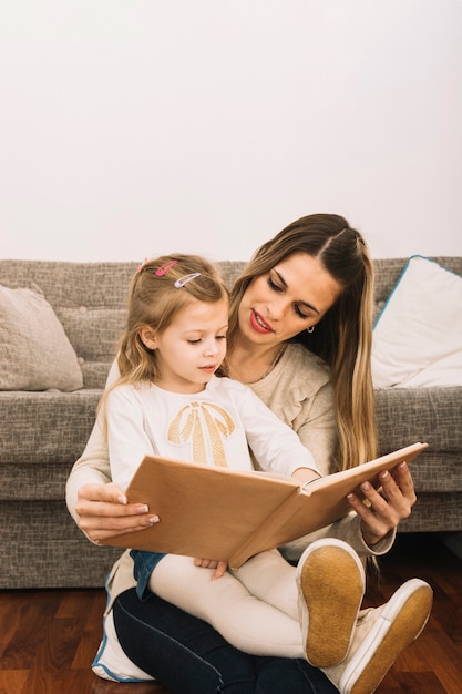 Young woman reading book to daughter near couch