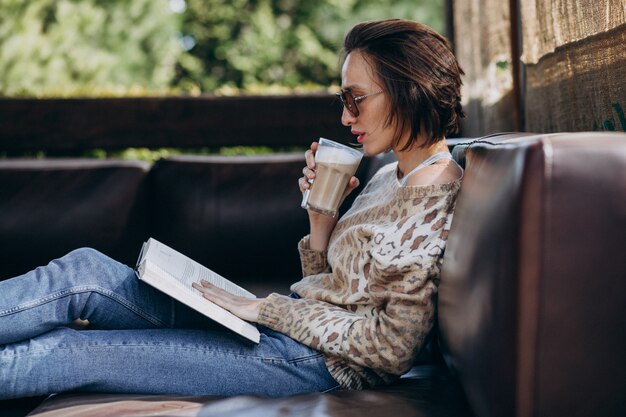 Молодая женщина читает книгу и пьет кофе