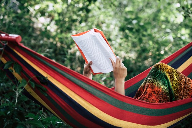 ハンモックに横たわっている本を読んでいる若い女性