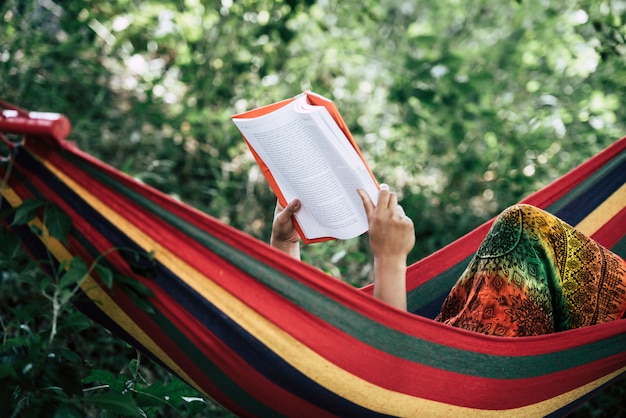 Young woman reading a book lying in a hammock